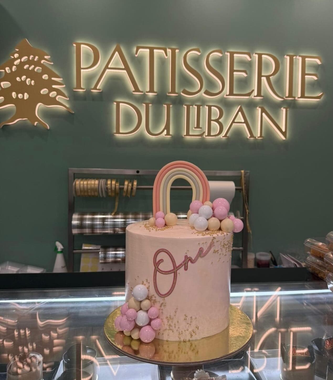 Pastel first birthday cake with rainbow topper at Patisserie Du Liban.
