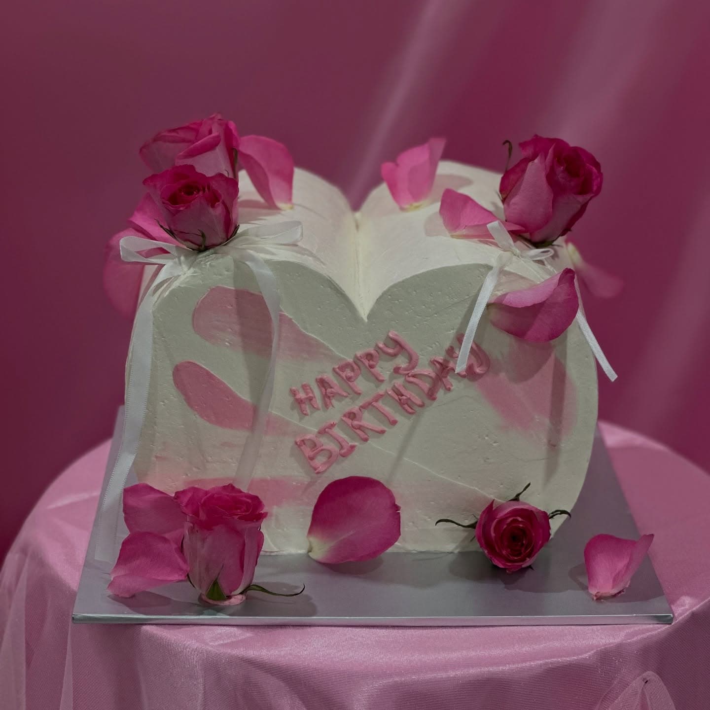 White heart-shaped birthday cake with pink roses.