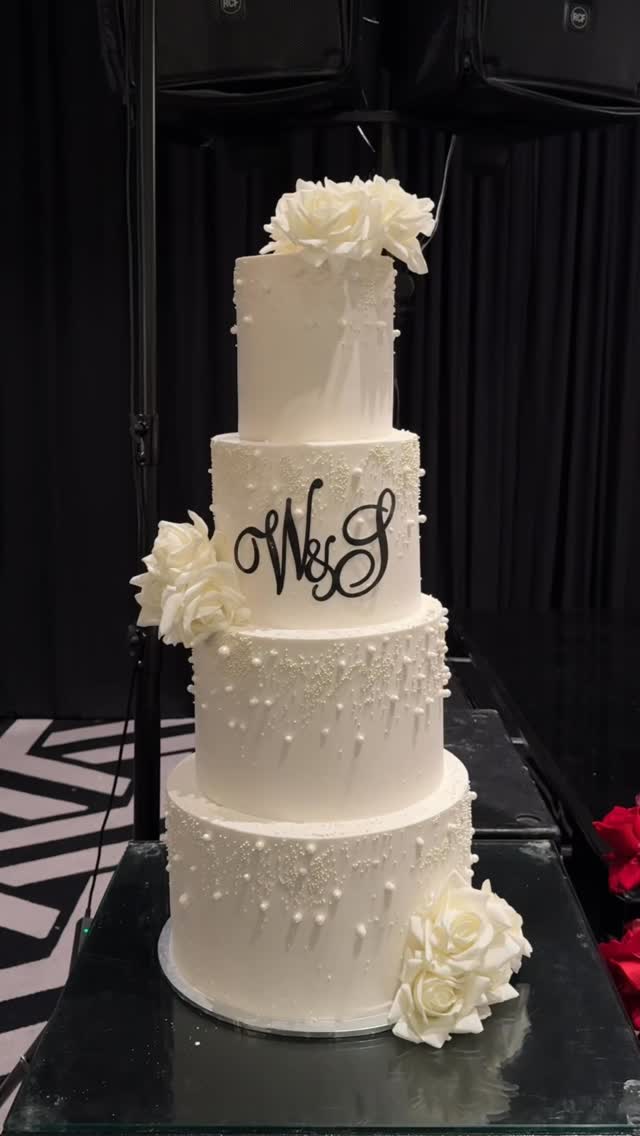 Four-tier white wedding cake with roses and monogram.